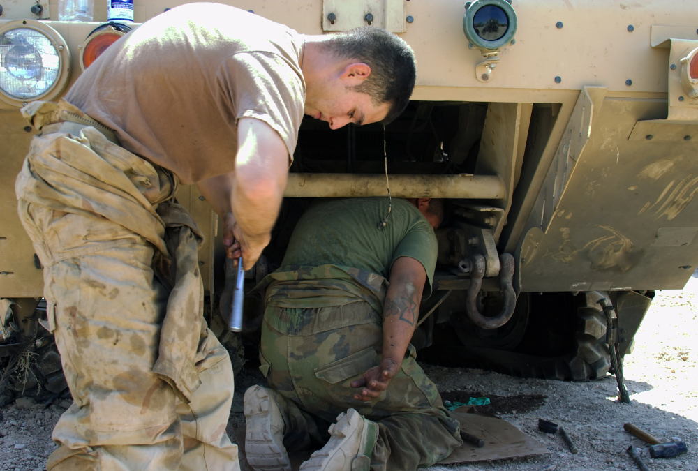Two people repairing a military vehicle.